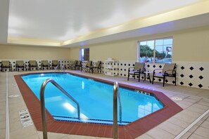 Une piscine avec une terrasse carrelée, un ensemble de chaises et une fenêtre donnant sur l’extérieur.