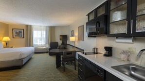 Una habitación de hotel con cama, escritorio, silla, kitchenette y baño.