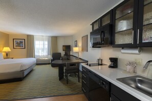 Una habitación de hotel con cama, escritorio, silla, kitchenette y baño.