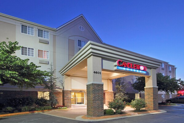 Un hôtel doté d’une entrée imposante, d’une enseigne indiquant « Candlewood Suites » et d’une voie d’accès pour les véhicules d’urgence marquée sur le trottoir.