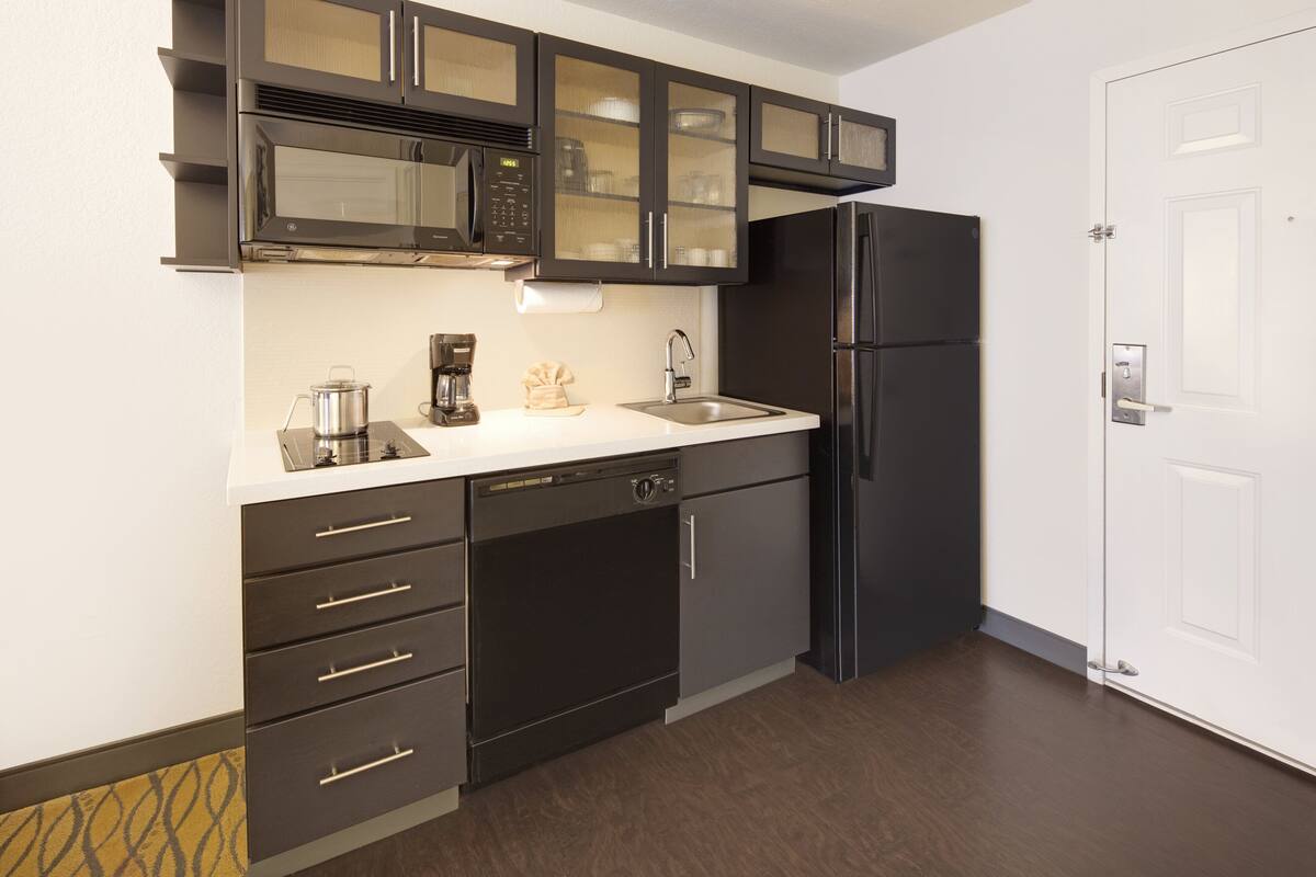 A modern kitchen with dark cabinetry, a stainless steel refrigerator, and a microwave.