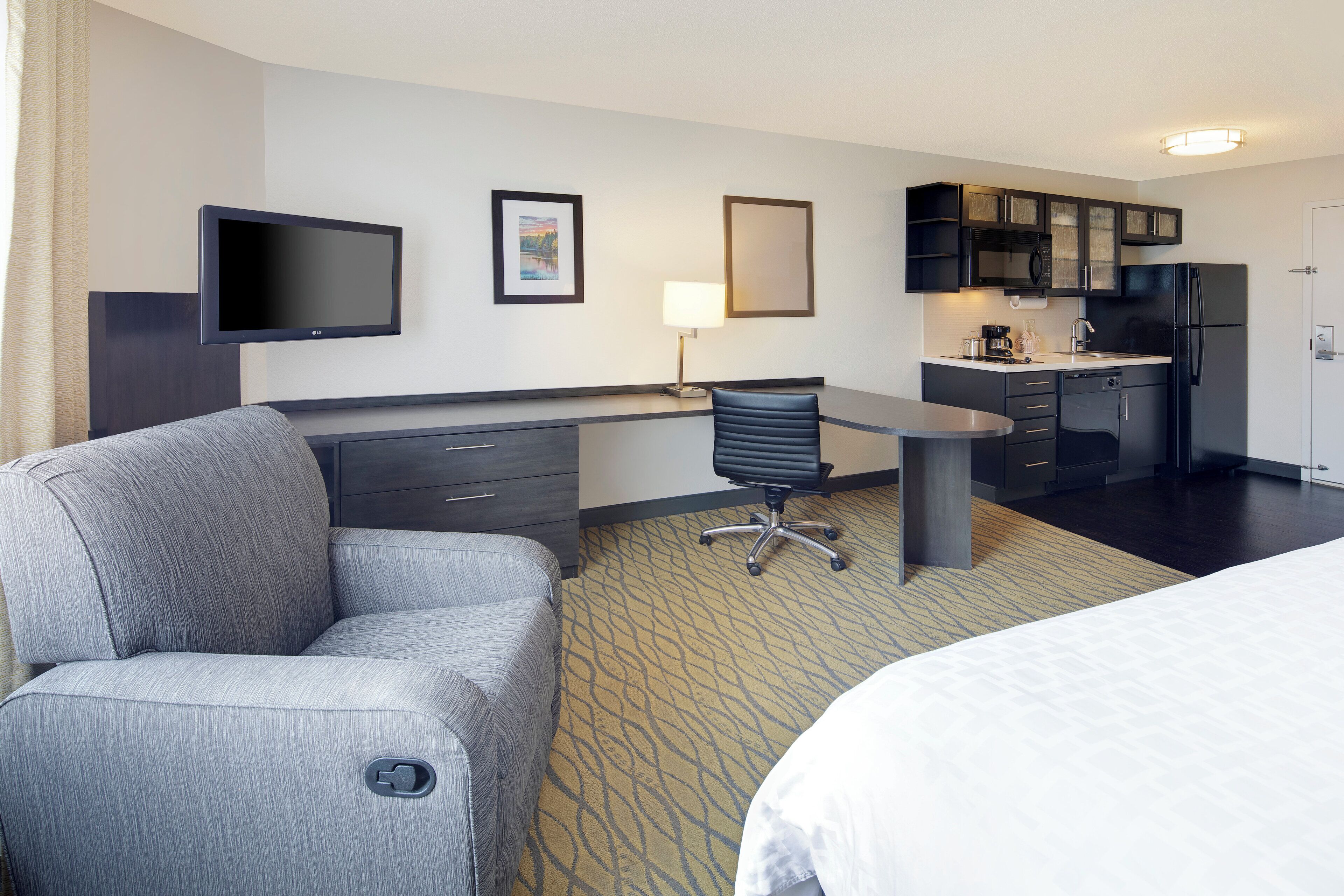 Habitación de hotel con cama, escritorio, silla, televisión, zona de cocina y baño.