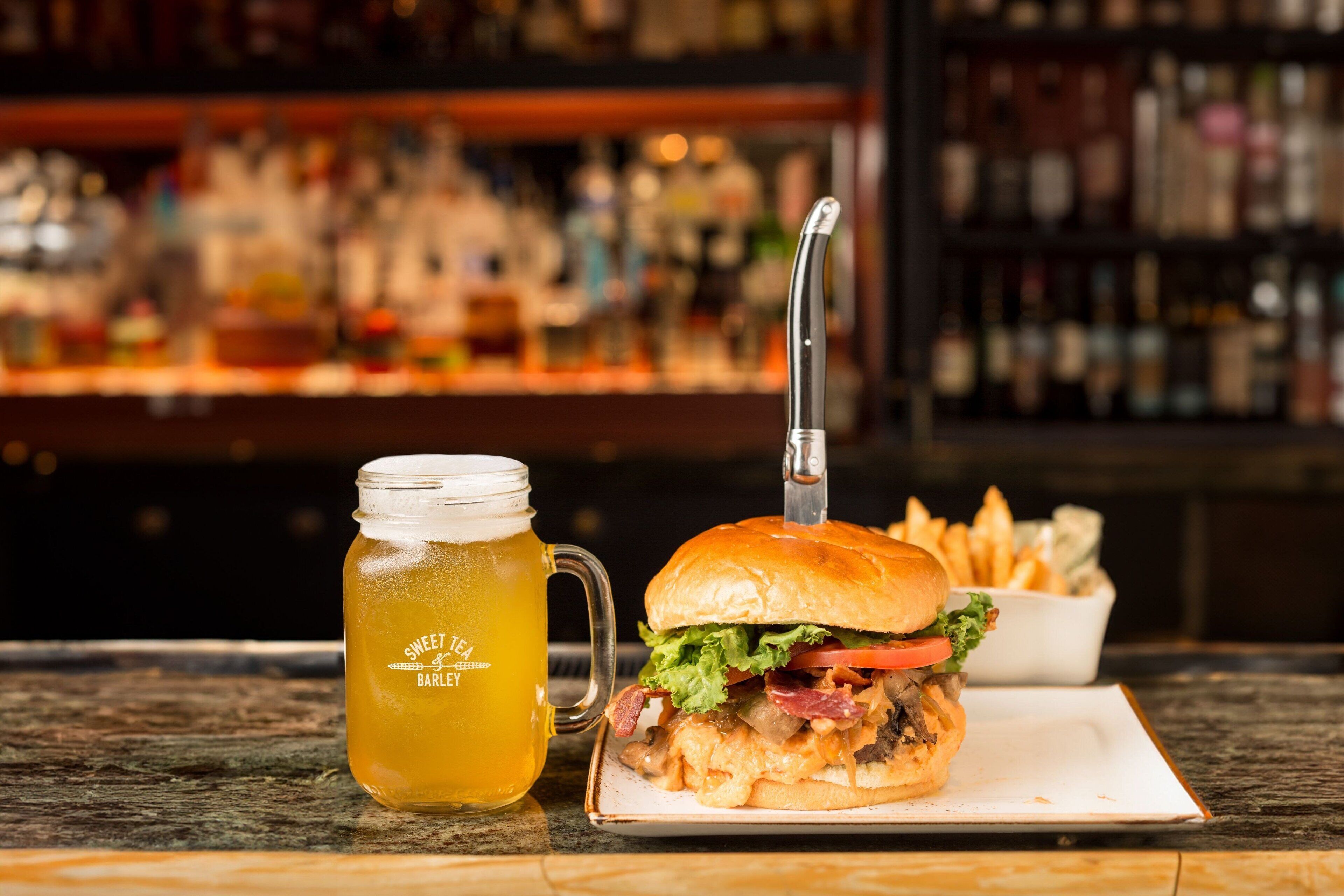 A meal with a burger and fries, a beer mug, and a bar in the background.