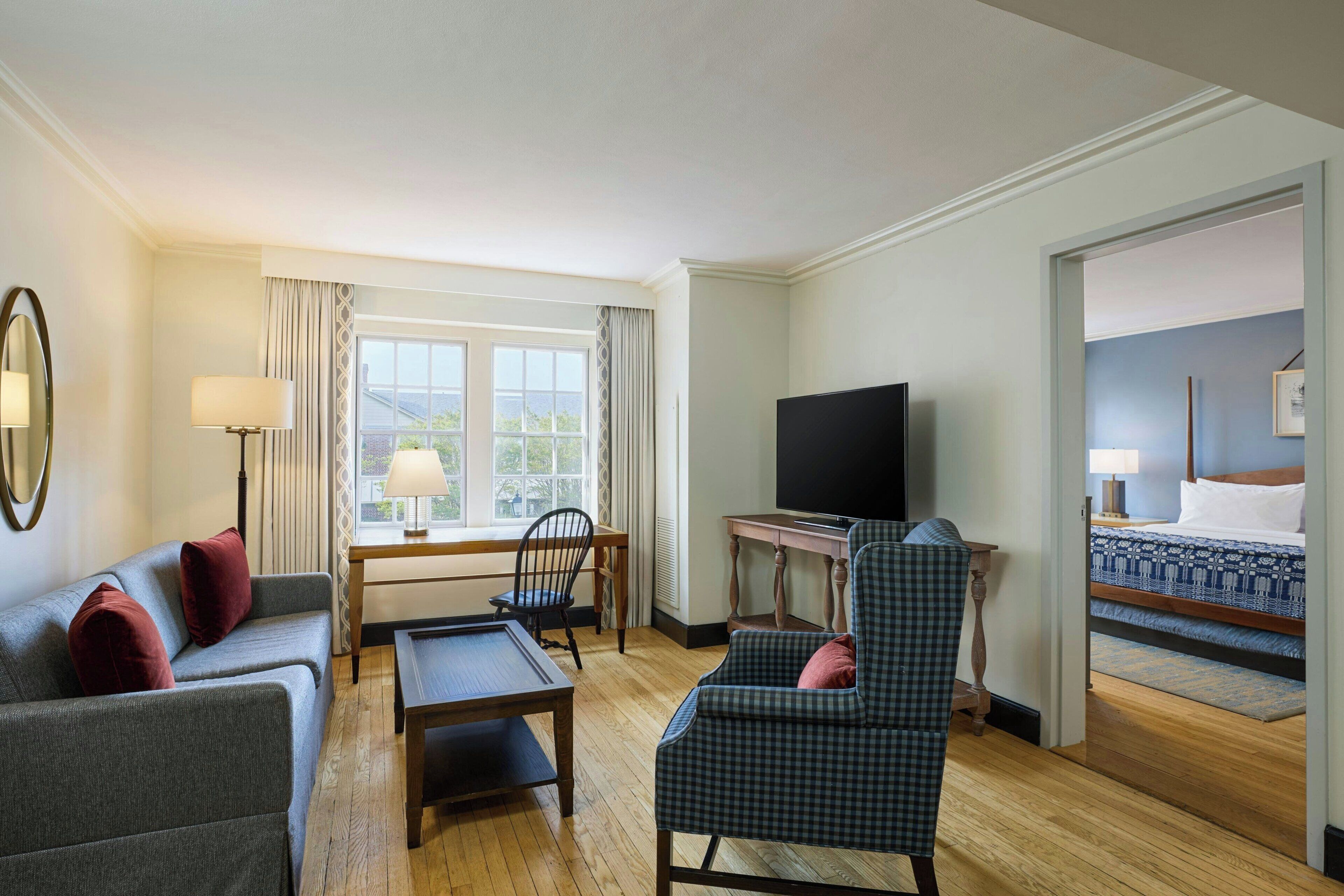 A hotel room with a sofa, armchair, desk, television, and a bed with a patterned bedspread.