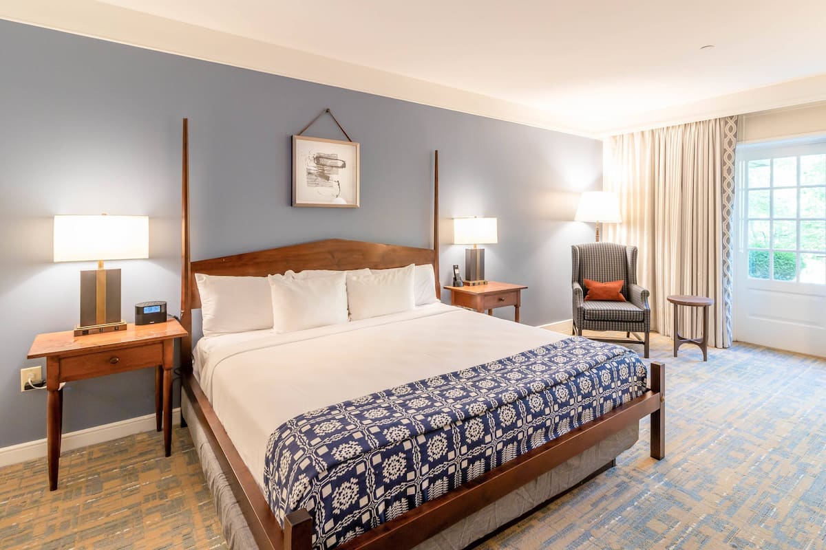 A hotel room with a large bed, two bedside tables, a chair, and a window with curtains.