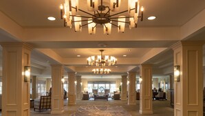 Eine geräumige Lobby mit einem großen Chandelier, hohen Decken und einem gemusterten Teppich.