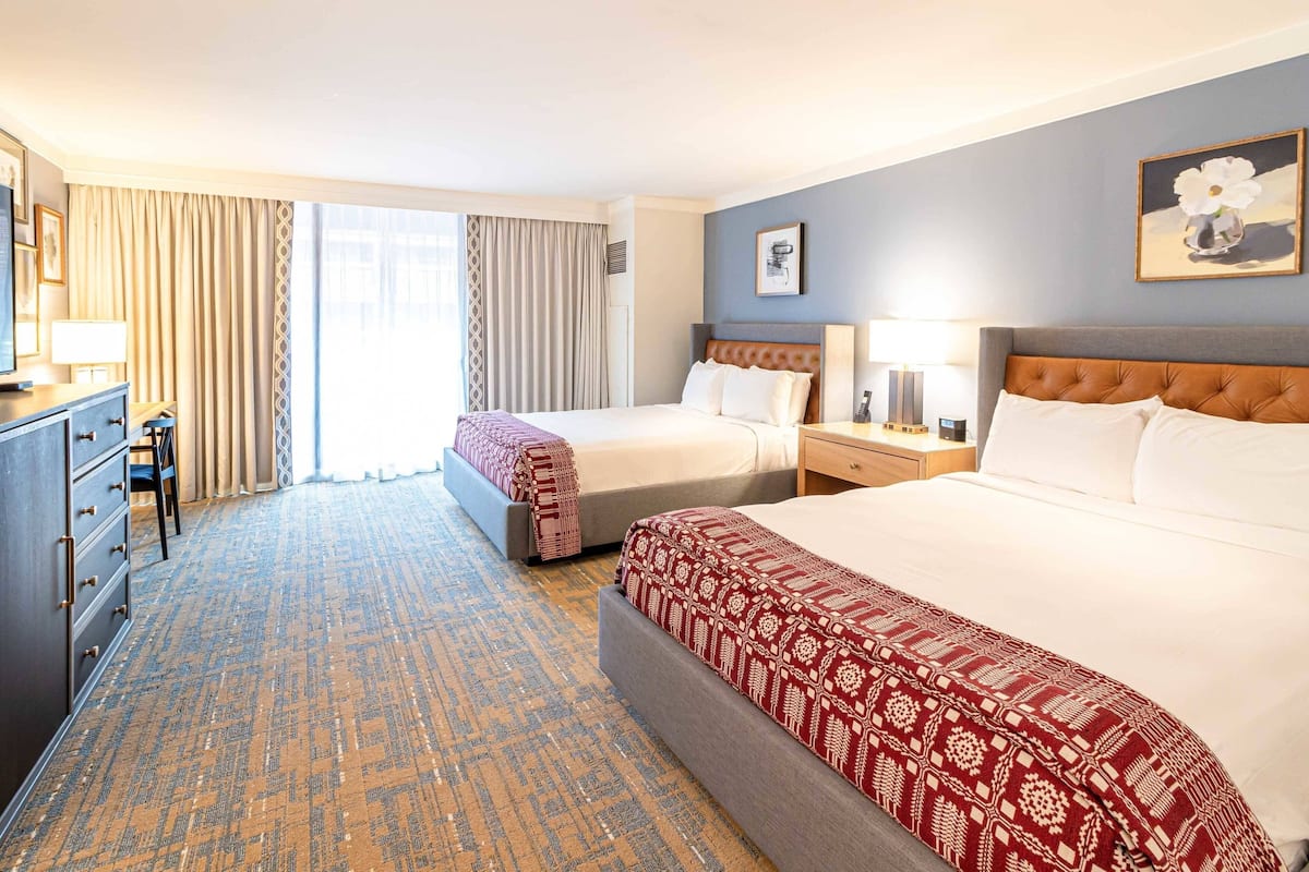 A hotel room with two beds, a desk, and a large window with curtains.