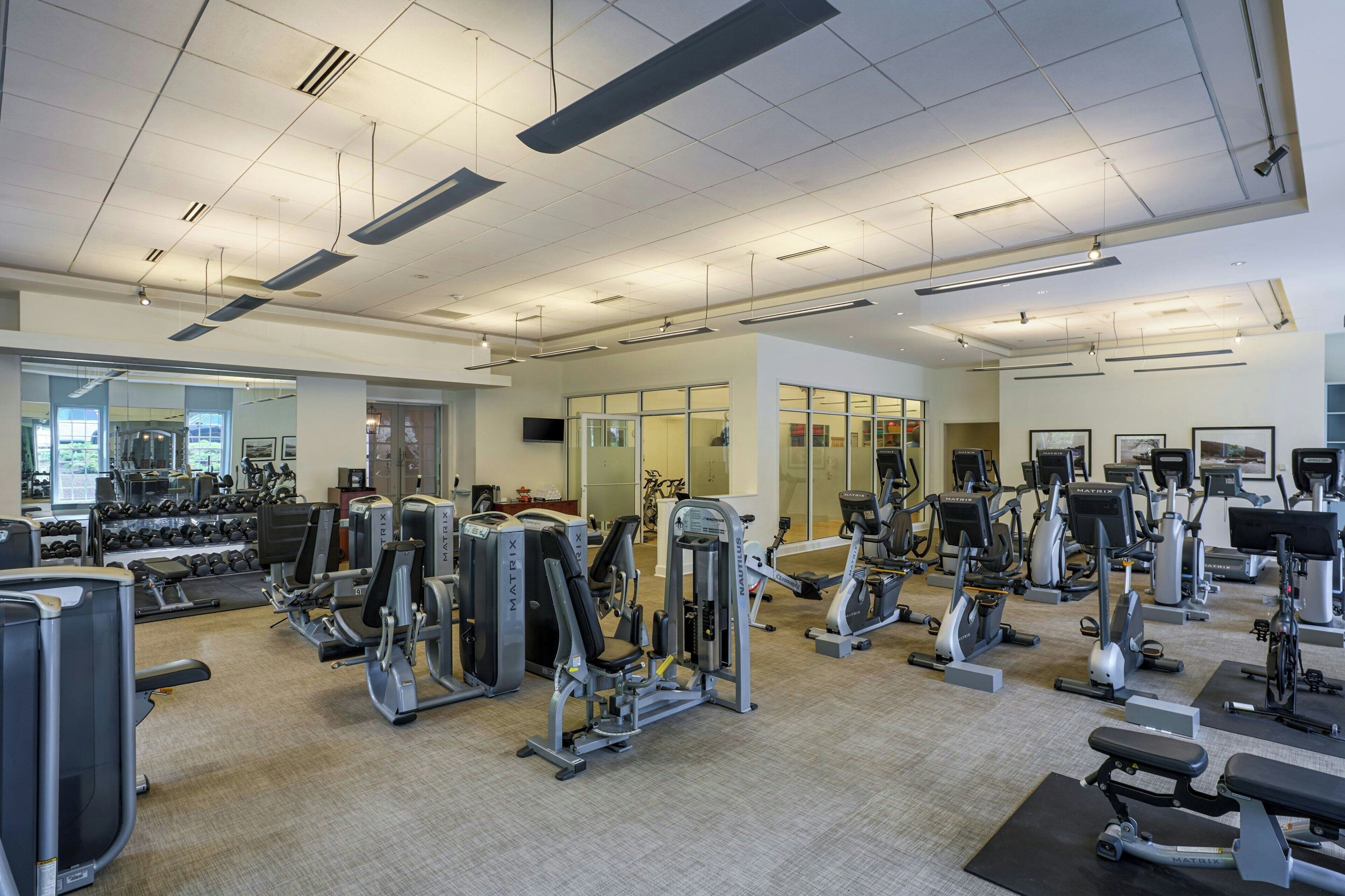 A gym with various exercise machines, mirrors, and a large window.