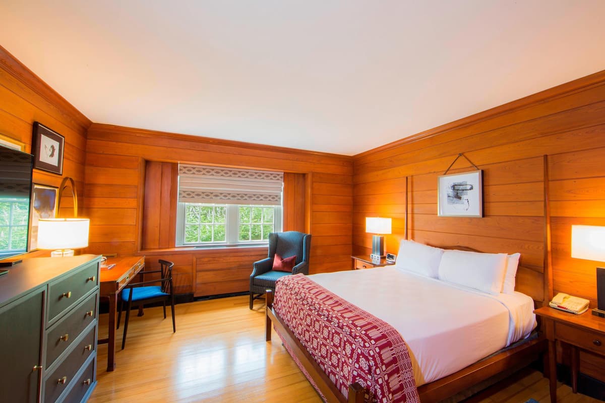 A wooden-paneled room with a bed, desk, chair, and dresser.