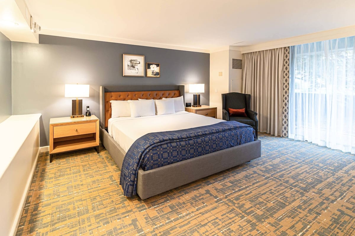 A hotel room with a large bed, two bedside tables, a chair, and a large window with curtains.