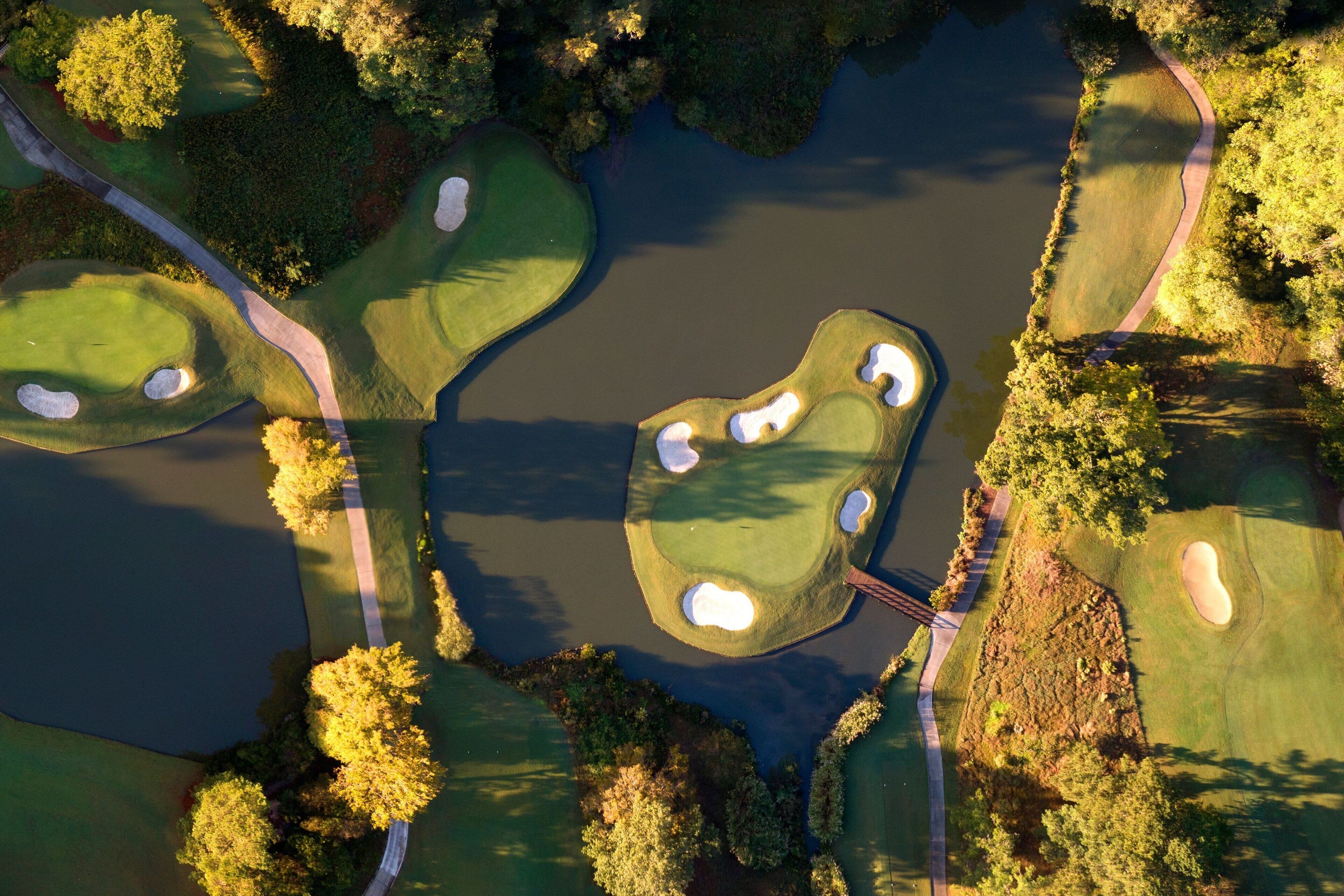 Vue aérienne d’un parcours de golf avec de nombreux bunkers, des obstacles d’eau et un pont.