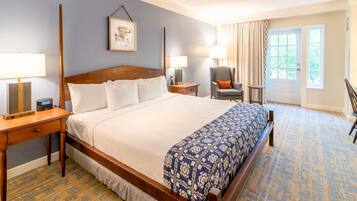 Habitación de hotel con una cama grande, dos mesitas de noche con lámparas, una silla, una puerta con vistas y una alfombra estampada.