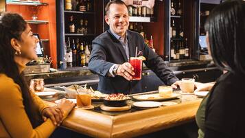 A bar setting with a bartender serving a drink, a woman in a yellow sweater, and a man in a suit.