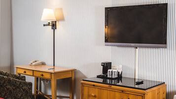 A hotel room with a flat-screen TV, a desk with a lamp, a telephone, a coffee maker, and a cabinet.