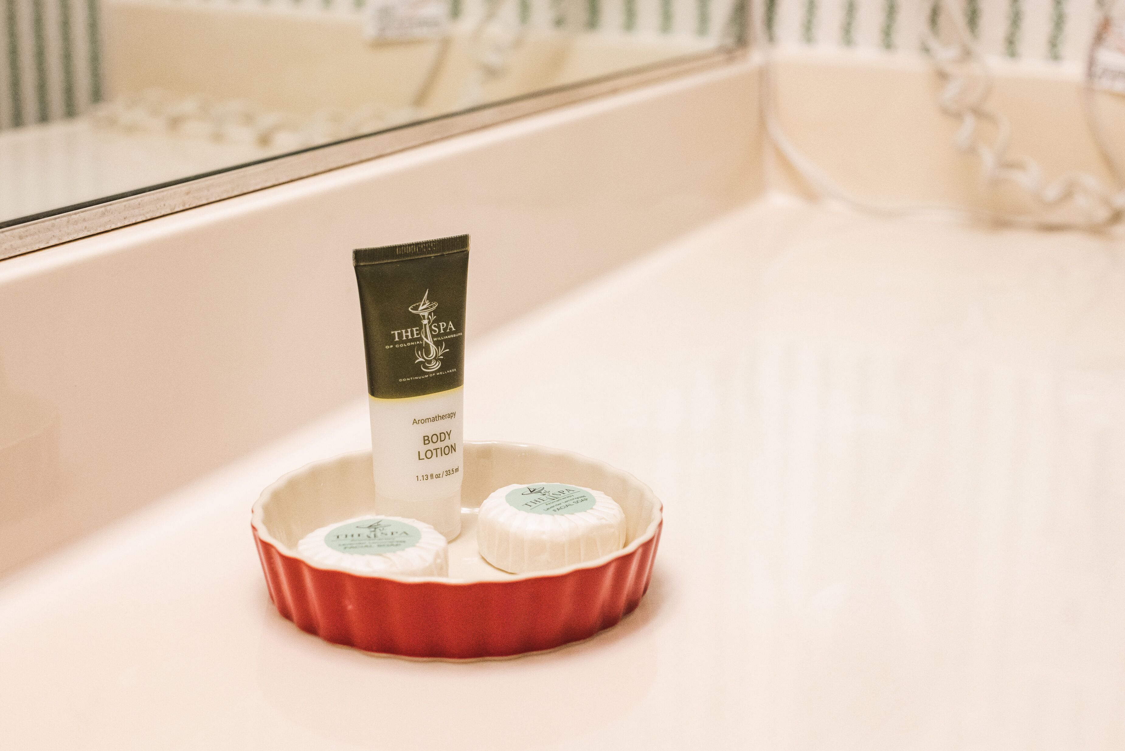 Un baño con un lavamanos blanco, un jabonera roja y una botella de crema corporal aromática The Spa.