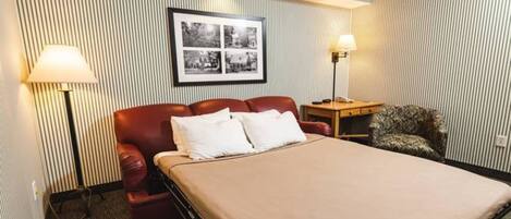 A hotel room with a bed, a desk, a chair, a lamp, and a framed picture on the wall.