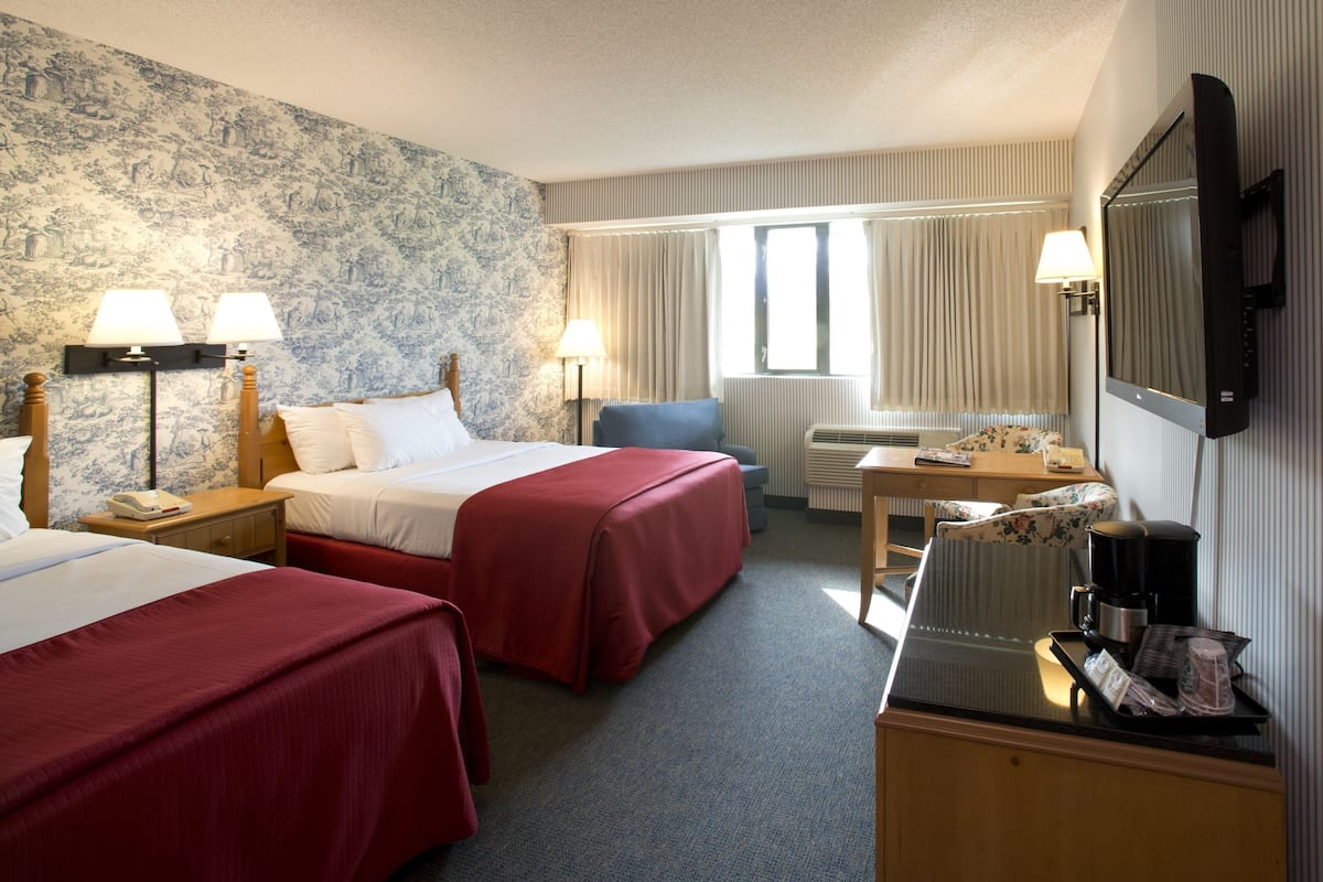 Une chambre d’hôtel avec deux lits, un bureau avec une machine à café, une chaise, une télévision et une fenêtre avec des rideaux.