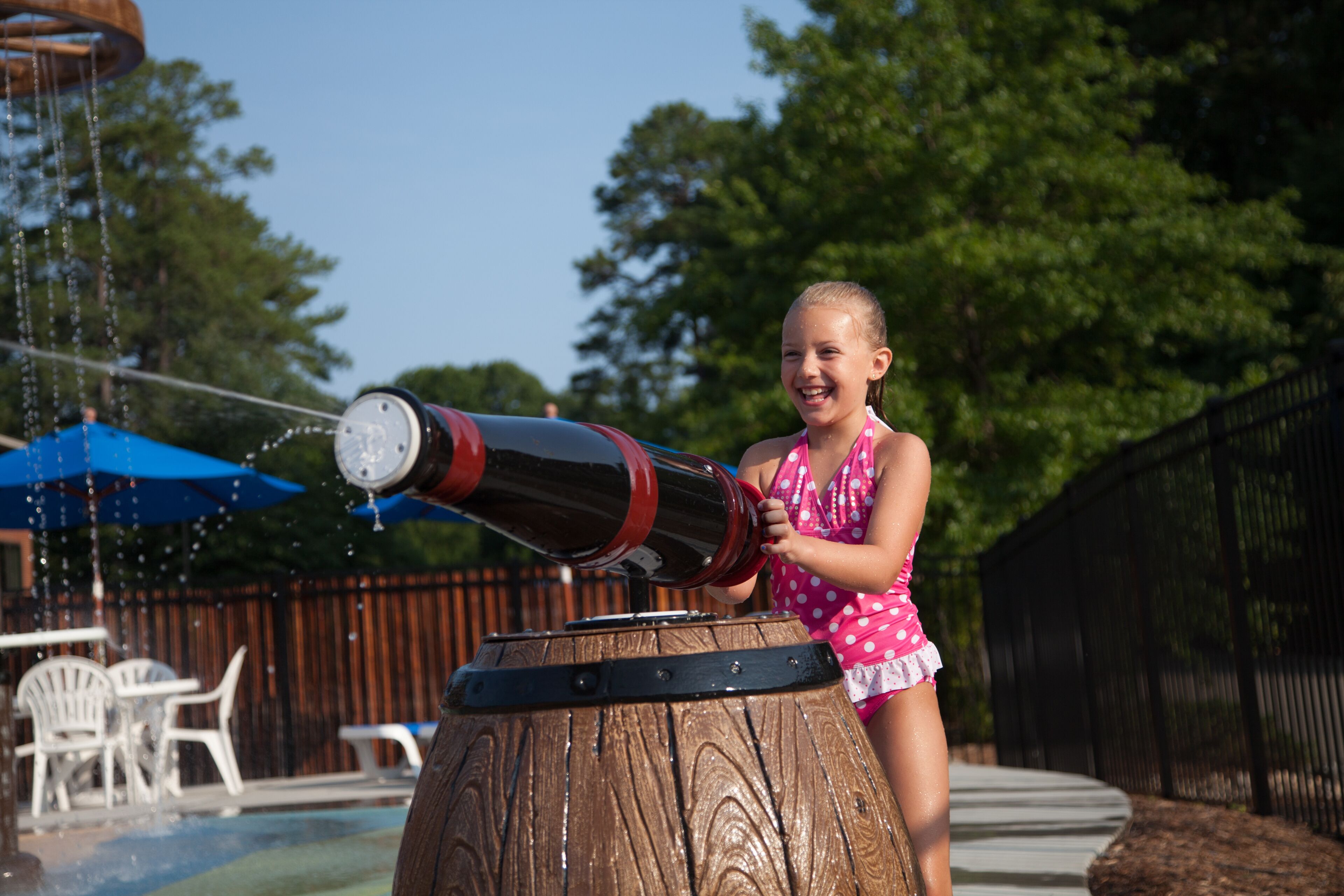 A child in a polka dot swimsuit operating a water cannon.