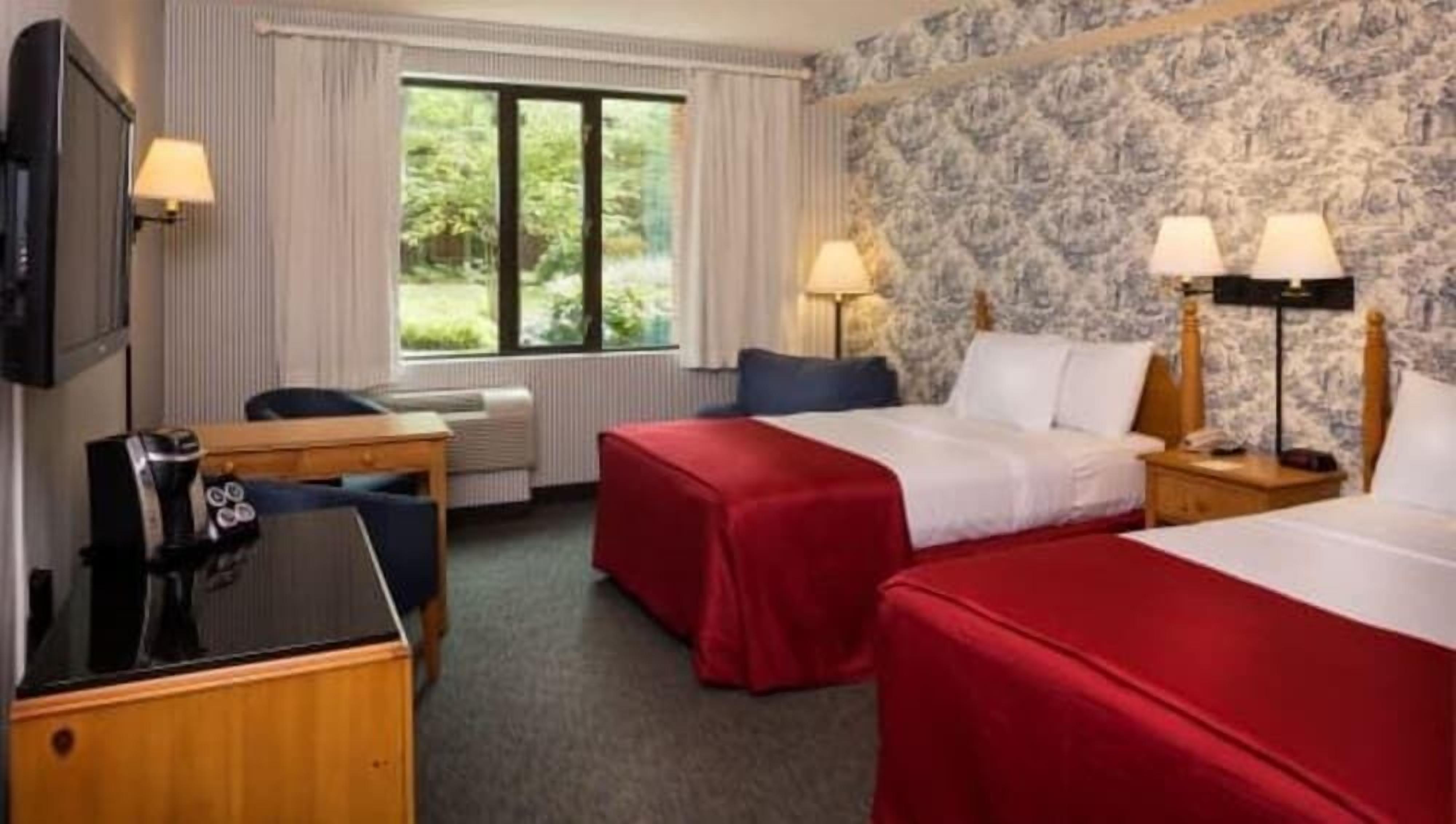 Hotellihuone, jossa on kaksi sänkyä, työpöytä, tuoli, televisio ja ikkuna, josta on näkymä vehreään maisemaan.