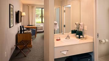 A hotel room with a large mirror, a sink, a chair, a desk, and a window.