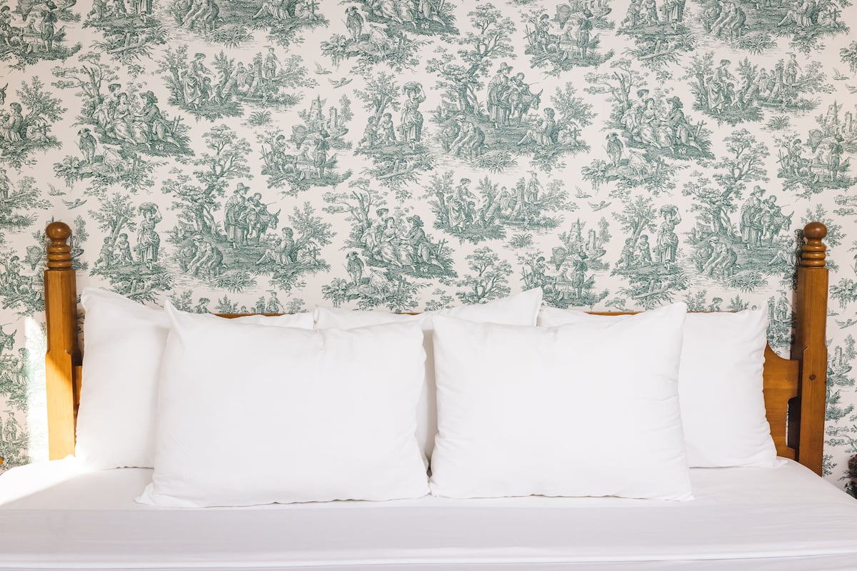 Un lit avec une literie blanche et une tête de lit adossée à un papier peint orné d’un motif botanique vert.