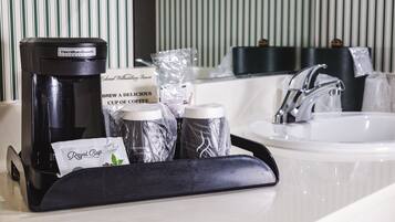 Baño de hotel con cafetera, cápsulas de café y un paquete de café Royal Cup.