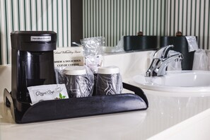 A hotel bathroom with a coffee maker, coffee pods, and a Royal Cup coffee bag. - Williamsburg Woodlands Hotel & Suites, an official Colonial Williamsburg Hotel (Williamsburg)