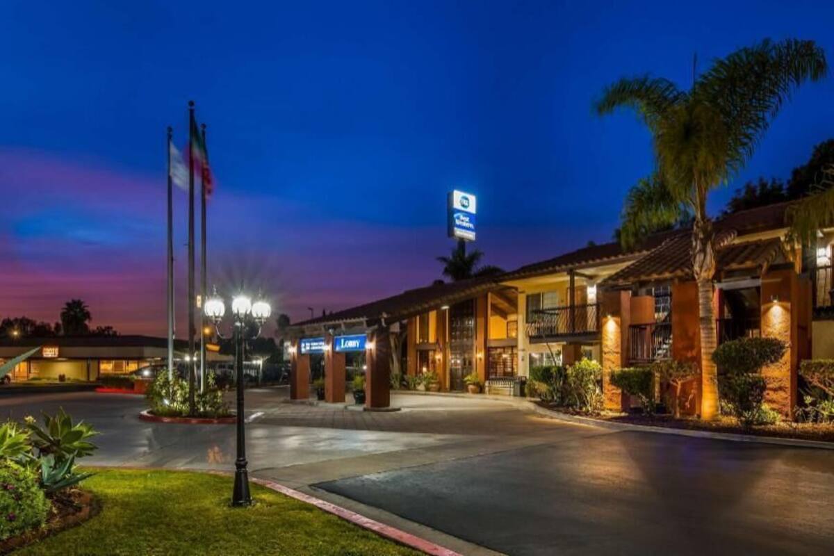 A hotel entrance with a well-lit facade, palm trees, and a clear sky.