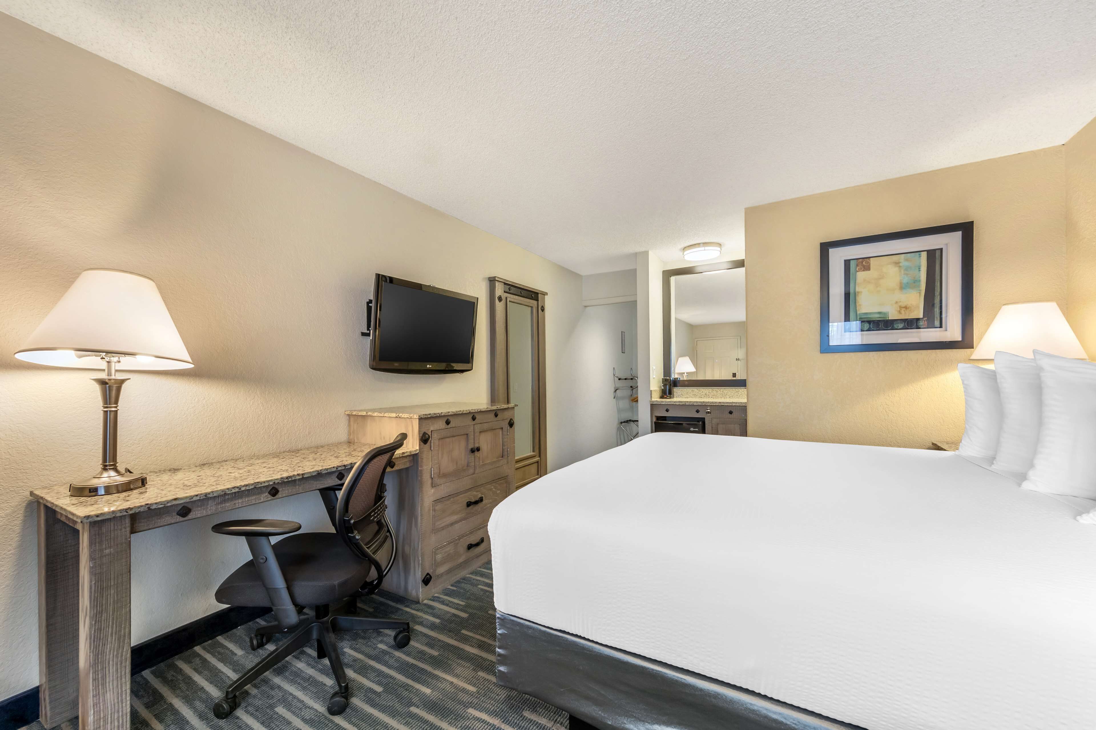 A hotel room with a bed, desk, chair, television, and a painting on the wall.