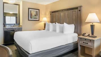 A hotel room with a large bed, two bedside lamps, a nightstand with a phone, a small desk with a lamp, and a mirror above the desk.