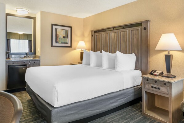 A hotel room with a large bed, two bedside lamps, a nightstand with a phone, a small desk with a lamp, and a mirror above the desk.