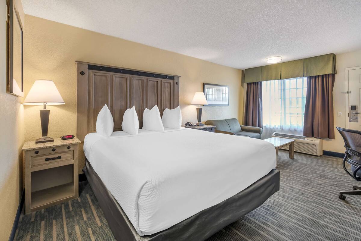 A hotel room with a large bed, two bedside tables with lamps, a desk, a chair, and a window with curtains.