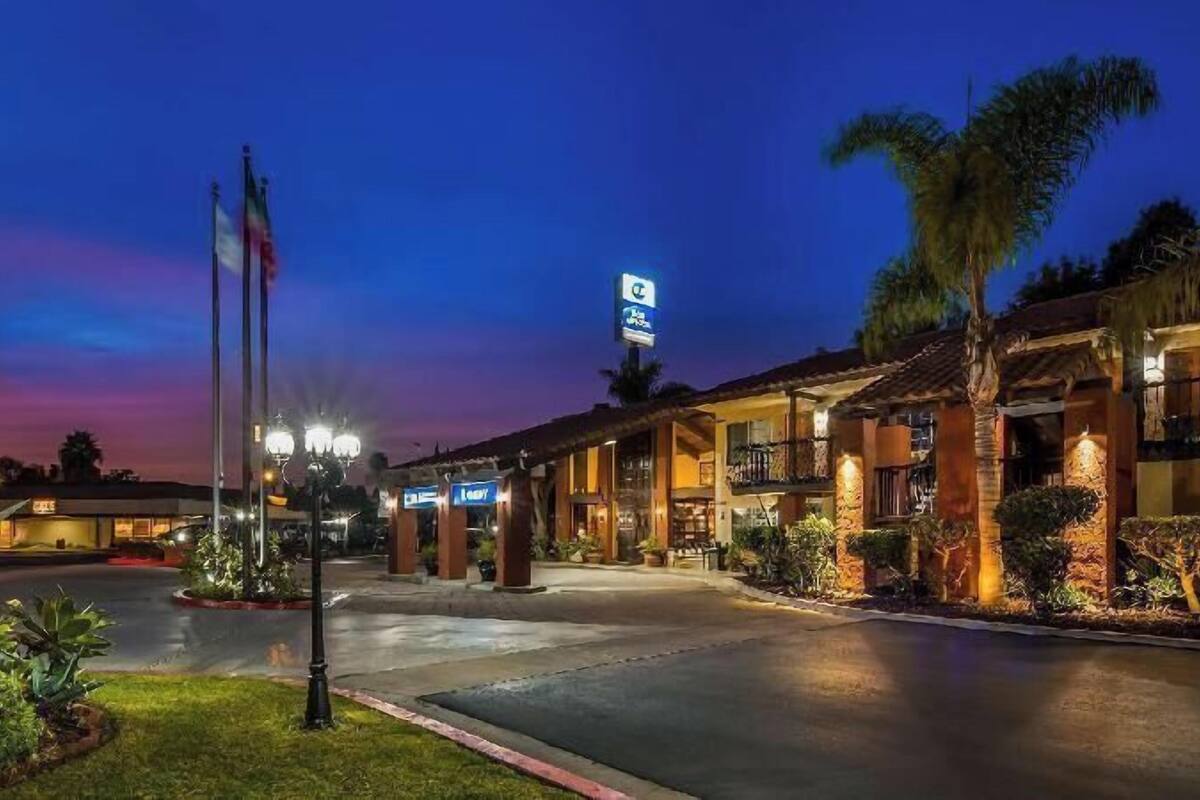 A hotel with a well-lit entrance, a signboard, and a landscaped garden.