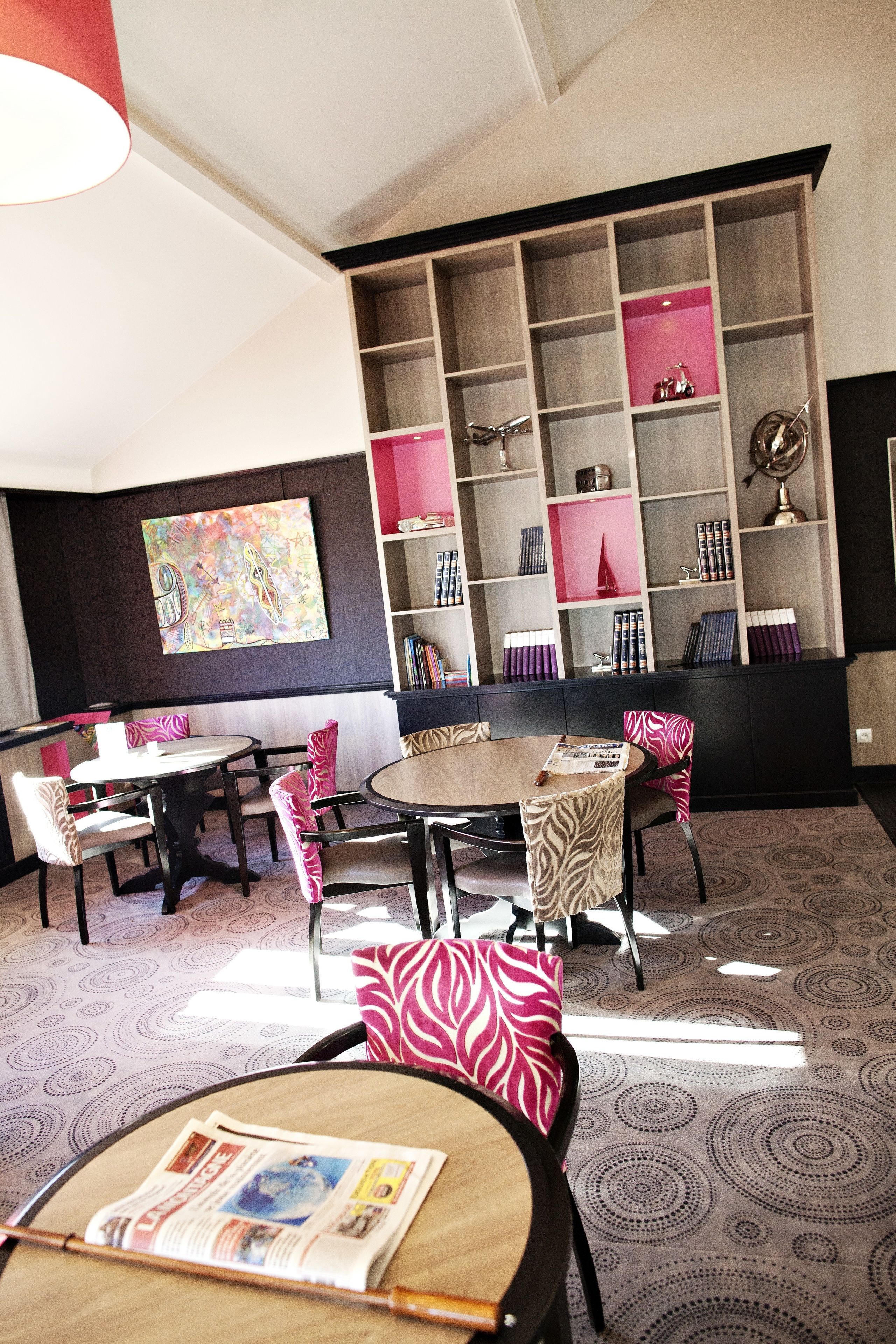 A modern library with bookshelves, a large painting, and a dining area with tables and chairs.