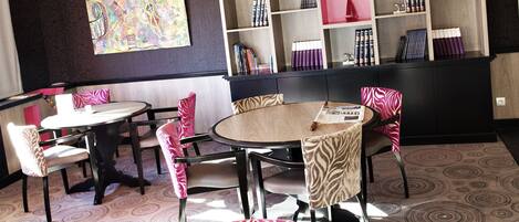 Una biblioteca moderna con estanterías, un cuadro grande y un área de comedor con mesas y sillas.