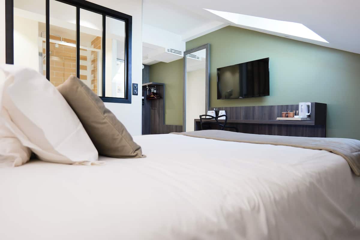 A hotel room with a large bed, a flat-screen TV mounted on the wall, a coffee machine, and a view of the outside through a window.