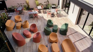 An outdoor seating area with tables and chairs, surrounded by plants and a wooden deck.