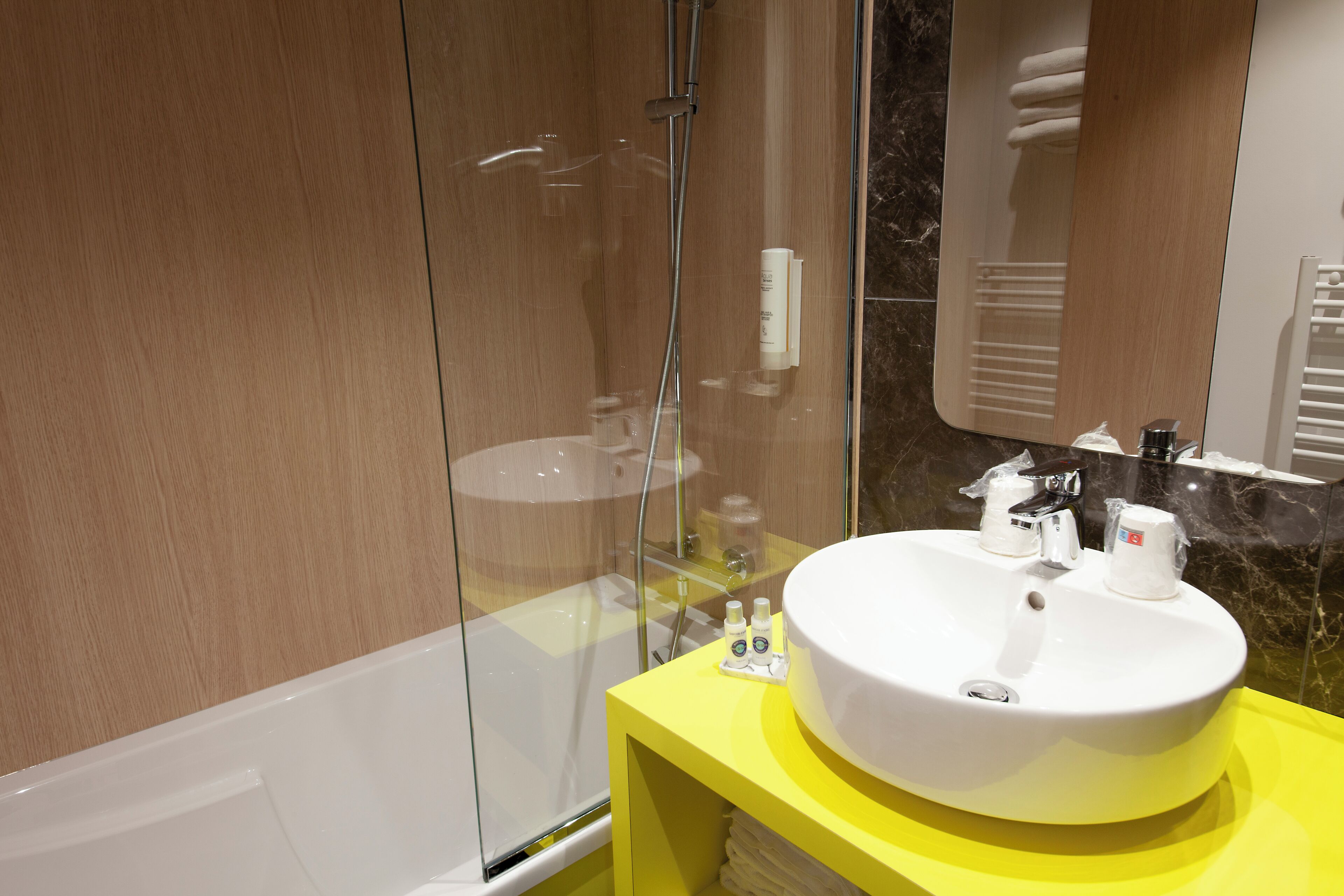 A modern bathroom with a glass shower enclosure, a white sink, and a yellow vanity.