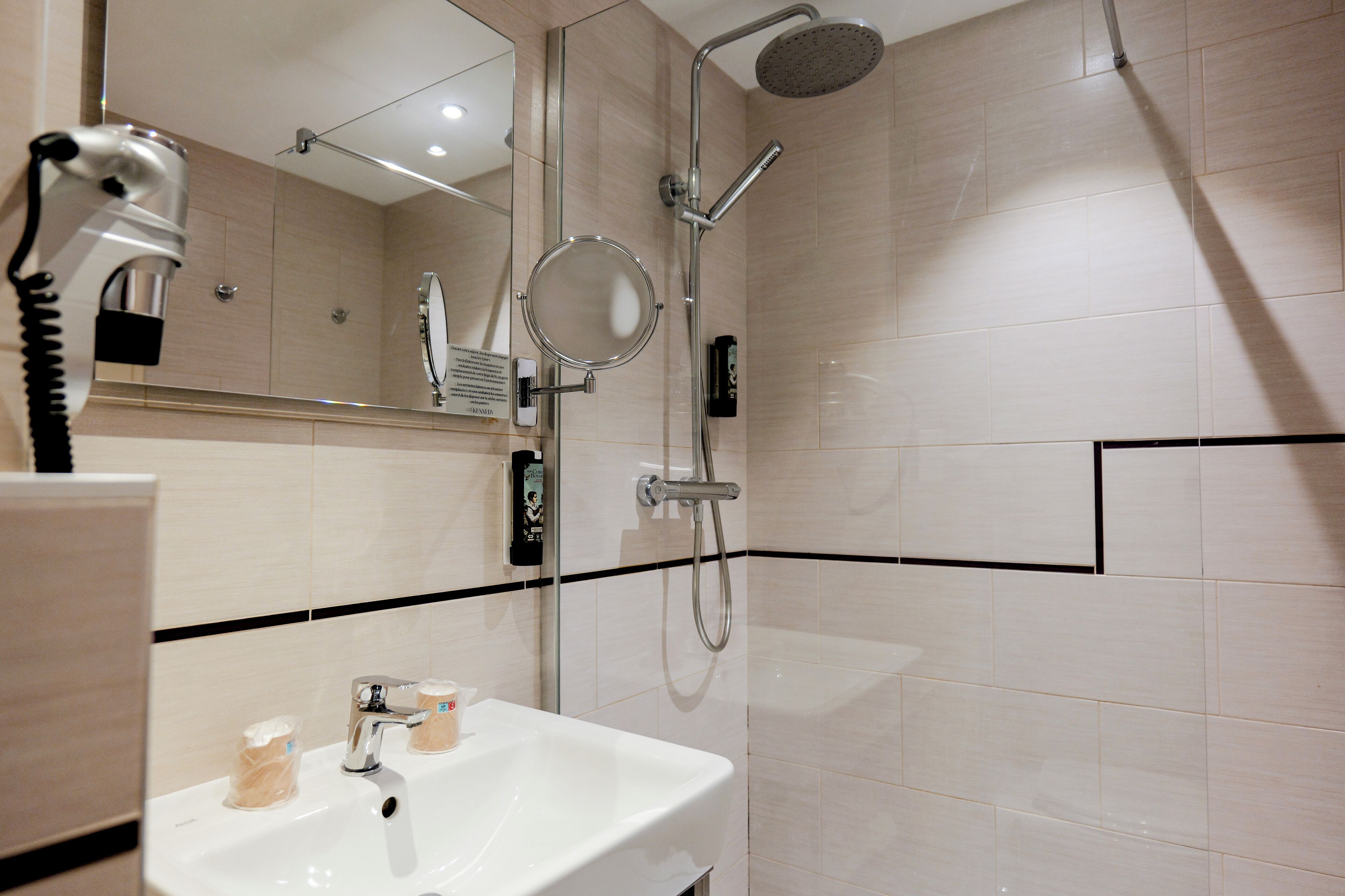 A modern bathroom with a white sink, a handheld showerhead, a wall-mounted mirror, and a handheld hairdryer.