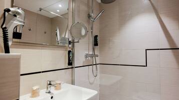 A modern bathroom with a white sink, a handheld showerhead, a wall-mounted mirror, and a handheld hairdryer.