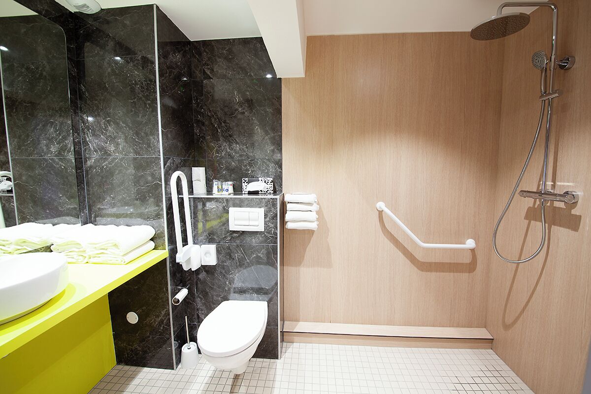 A modern bathroom with a marble vanity, a toilet, a shower with a grab bar, and a wooden door.