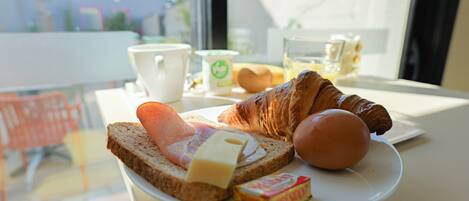 Un plato de desayuno con croissant, queso, jamón y otro croissant sobre una mesa con una taza y un vaso.