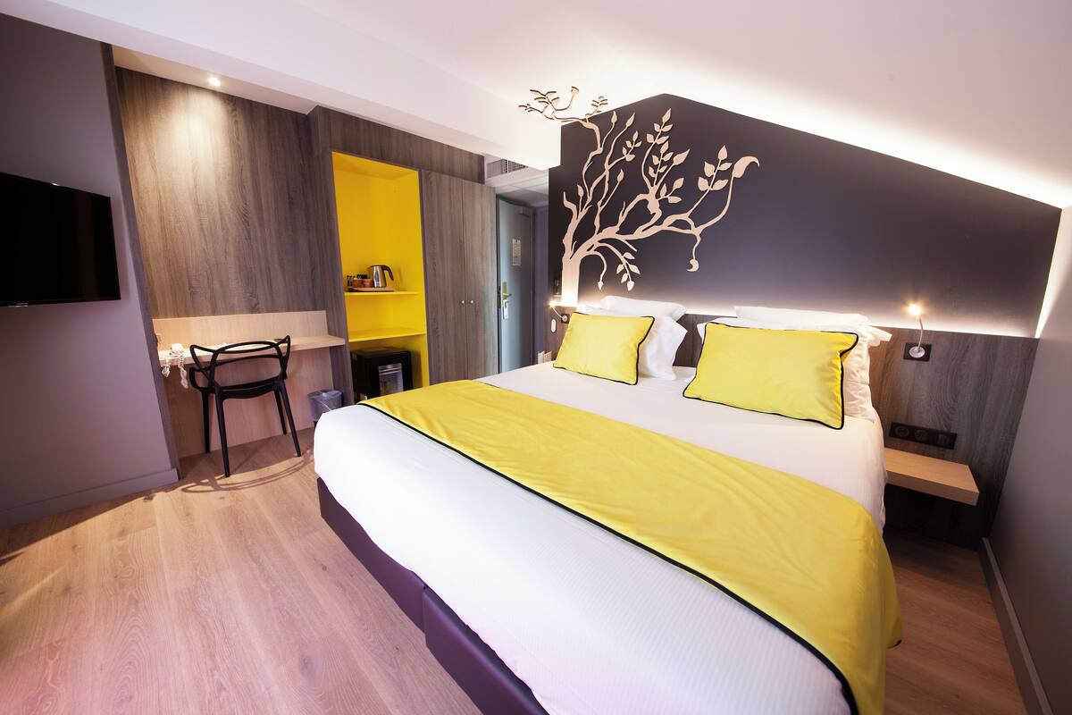 Een moderne hotelkamer met een groot bed, een aan de muur bevestigde televisie, een bureau met stoel en een garderobe.