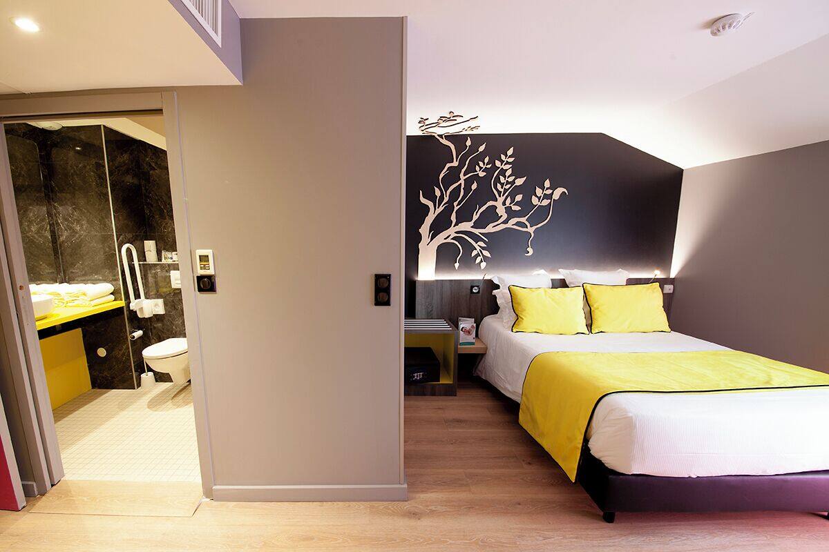 Een moderne hotelkamer met een bed, nachtkastje en een decoratieve boom aan de muur.