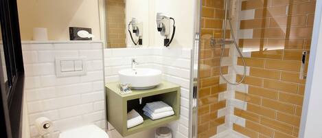 Un baño con inodoro blanco, lavabo con encimera verde y zona de ducha con azulejos marrones.
