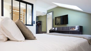 A hotel room with a large bed, a flat-screen TV mounted on the wall, a coffee machine, and a view of the outside through a window.