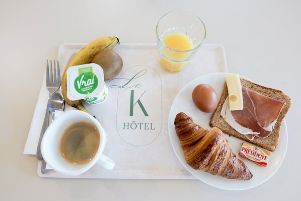 A breakfast tray with a croissant, ham, cheese, egg, banana, yogurt, juice, and coffee.