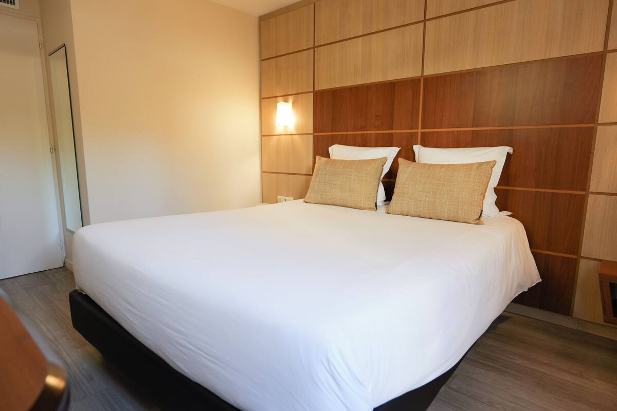 Een hotelkamer met een groot bed, een houten hoofdbord en een nachtkastje met een lamp.