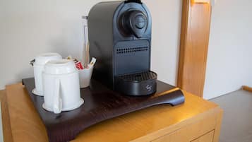 Una cafetera sobre una mesa de madera, con dos tazas blancas y un azúcar.