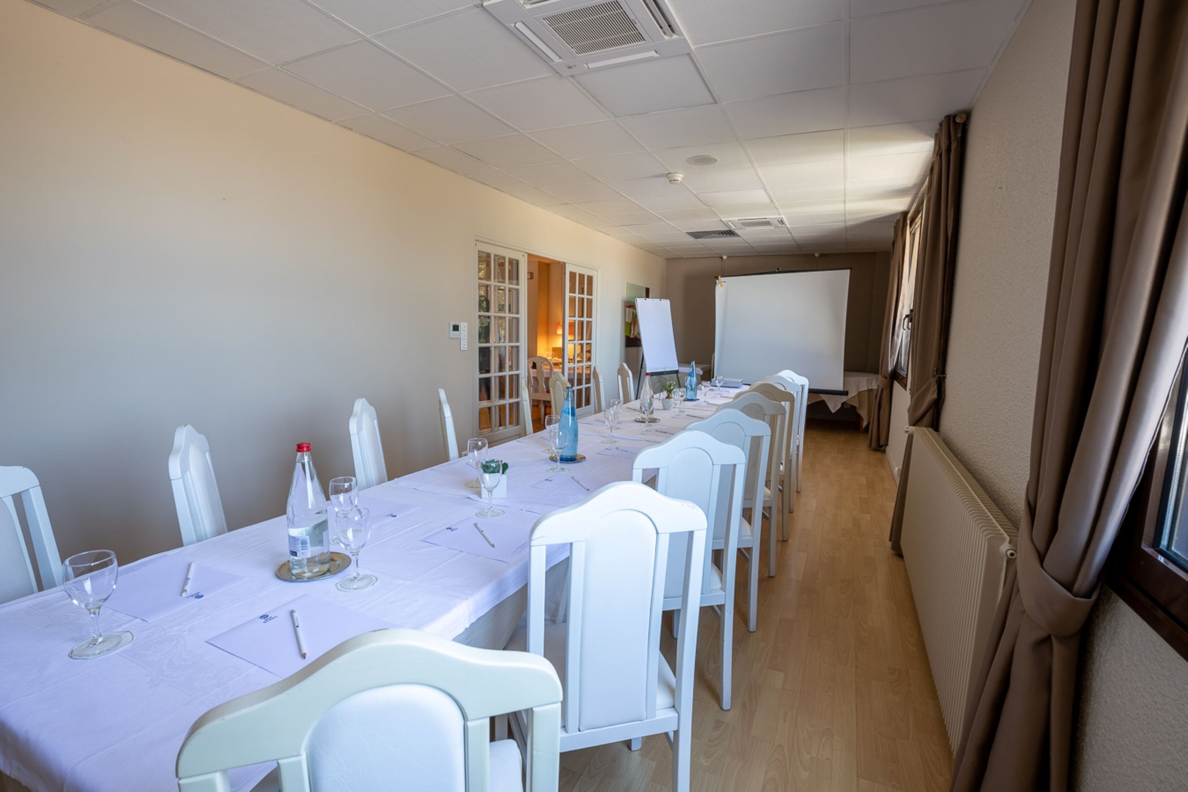 A conference room with a long table, white chairs, a whiteboard, and a projector screen.
